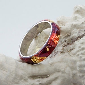 Puede incluir: Un anillo rojo y dorado con una banda plateada. El anillo est&aacute; hecho de resina y tiene un aspecto marmoleado &uacute;nico.