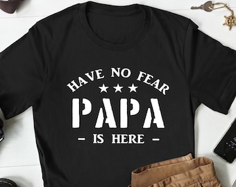 Pode incluir: Camiseta preta com texto branco que diz "Have No Fear Papa - Is Here -" com três estrelas acima da palavra "Papa".