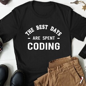 May include: Black t-shirt with white text that reads "The Best Days Are Spent Coding".
