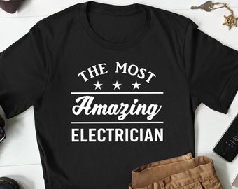 May include: Black t-shirt with white text that reads "The Most Amazing Electrician" with three stars above the word "Amazing".