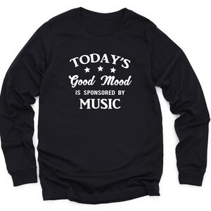 May include: Black long-sleeve t-shirt with white text that reads "TODAY'S Good Mood IS SPONSORED BY MUSIC" with three white stars above the word "Good".