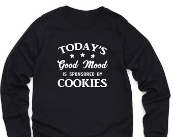 May include: Black long-sleeve t-shirt with white text that reads "TODAY'S Good Mood IS SPONSORED BY COOKIES" with three white stars above the word "Good".