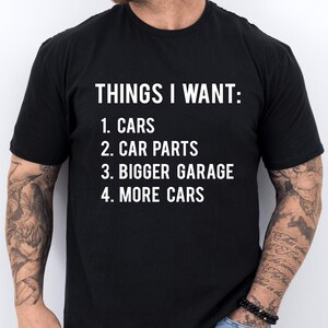May include: Black t-shirt with white text that reads "THINGS I WANT: 1. CARS 2. CAR PARTS 3. BIGGER GARAGE 4. MORE CARS"