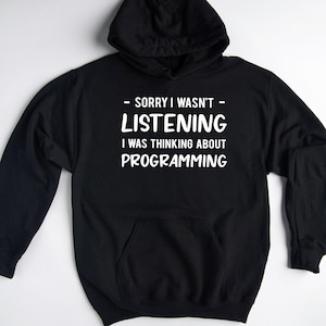May include: Black hooded sweatshirt with a front pocket and white text that reads "- SORRY I WASN'T LISTENING I WAS THINKING ABOUT PROGRAMMING". The sweatshirt has a drawstring hood.