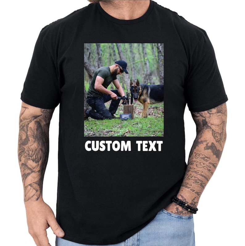 May include: Black t-shirt with a rectangular image of a person with a German Shepherd dog in a forest. The image has the words "CUSTOM TEXT" in white at the bottom. The person is kneeling and holding a tool.