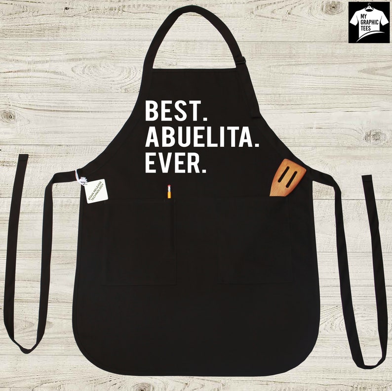May include: Black apron with a white text that says "BEST. ABUELITA. EVER.". The apron has a pocket with a wooden spatula inside.