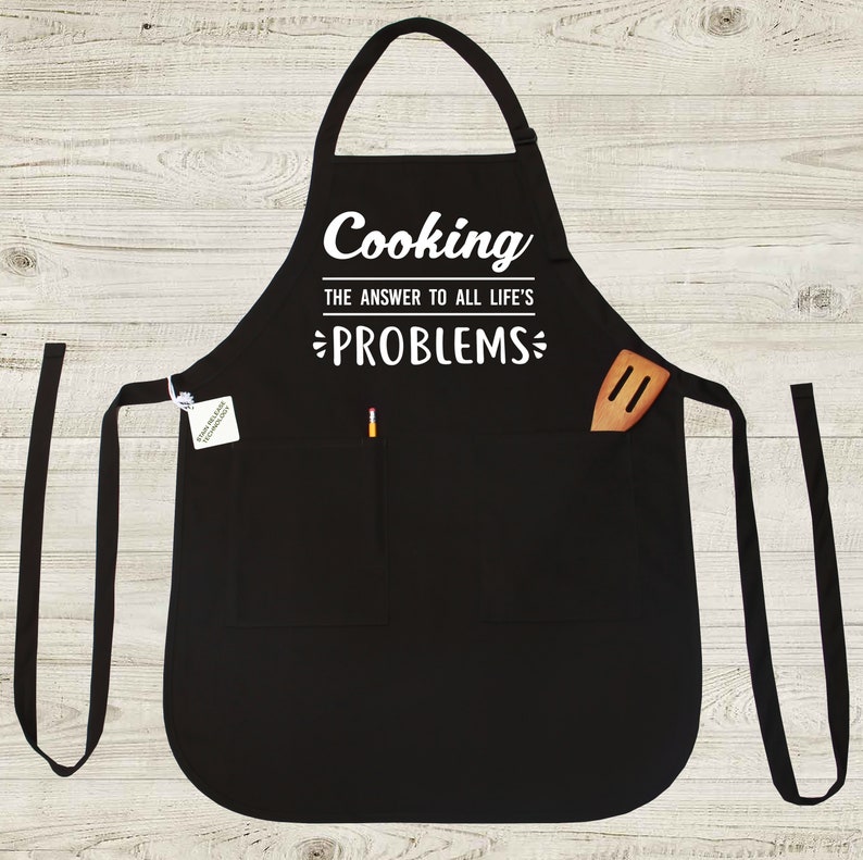 May include: Black apron with two pockets and a white graphic that reads "Cooking The Answer To All Life's Problems".