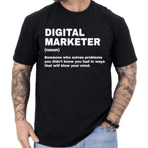 May include: Black t-shirt with the text "DIGITAL MARKETER (noun) Someone who solves problems you didn't know you had in ways that will blow your mind." The text is in white, centered on the shirt.