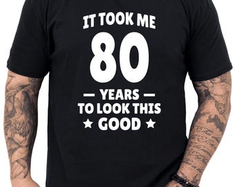 May include: Black t-shirt with white text that reads "It took me 80 years to look this good."  The text is surrounded by two white stars.