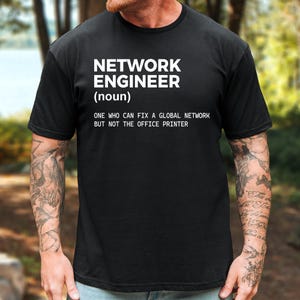 May include: A black short-sleeved t-shirt featuring white text that reads: NETWORK ENGINEER (noun) ONE WHO CAN FIX A GLOBAL NETWORK BUT NOT THE OFFICE PRINTER. The shirt has a crew neckline and a standard fit, displaying the printed graphic on the chest.