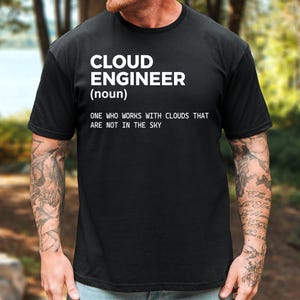 May include: A black short-sleeved t-shirt featuring white text that reads: CLOUD ENGINEER (noun) ONE WHO WORKS WITH CLOUDS THAT ARE NOT IN THE SKY. The shirt has a crew neckline and a standard fit, displaying the printed definition clearly on the chest.