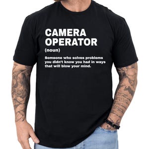 May include: Black crew neck t-shirt with the text "CAMERA OPERATOR (noun) Someone who solves problems you didn't know you had in ways that will blow your mind." The text is in white.