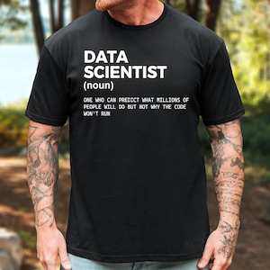 May include: A black short-sleeved t-shirt featuring white text that reads: DATA SCIENTIST (noun) ONE WHO CAN PREDICT WHAT MILLIONS OF PEOPLE WILL DO BUT NOT WHY THE CODE WON'T RUN. The shirt has a crew neckline and a standard fit design.