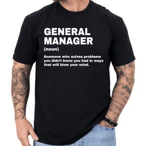 May include: Black t-shirt with the text "GENERAL MANAGER (noun) Someone who solves problems you didn't know you had in ways that will blow your mind." The text is in white, centered on the shirt.