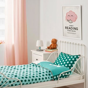 K&ouml;nnte beinhalten: Ein wei&szlig;es Metallbett mit einer t&uuml;rkis-wei&szlig;en Polka-Dot-Bettdecke und einem Kissen. Der Raum hat rosa Vorh&auml;nge, einen wei&szlig;en Nachttisch und einen gerahmten Druck mit der Aufschrift "Six minutes of READING are enough to reduce stress."