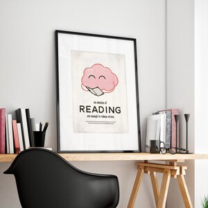 K&ouml;nnte beinhalten: Gerahmtes Poster mit dem Text "six minutes of READING are enough to reduce stress" und einer rosa Gehirngrafik. Das Poster befindet sich auf einem Holztisch mit einem schwarzen Stuhl, B&uuml;chern und einem Fenster mit Pflanzen.