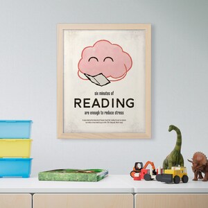 K&ouml;nnte beinhalten: Ein gerahmter Druck mit einem hellen Holzrahmen. Der Druck zeigt eine rosa Wolkenfigur, die ein Buch liest, mit dem Text "six minutes of READING are enough to reduce stress". Spielzeug befindet sich auf dem Regal darunter.