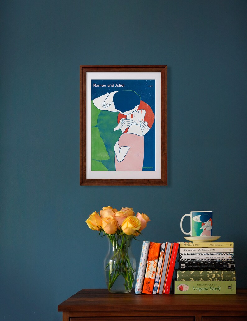 May include: A framed poster with a vintage illustration of a couple embracing. The poster is titled "Romeo and Juliet" and is displayed on a teal wall above a wooden table with a vase of yellow roses and a stack of books.