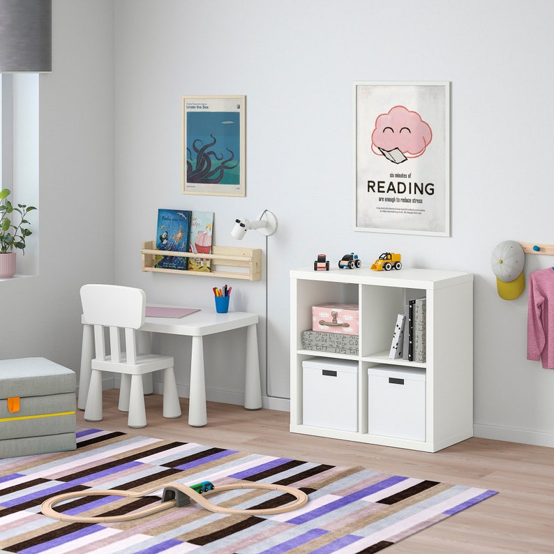 K&ouml;nnte beinhalten: Ein Kinderzimmer mit einem wei&szlig;en Schreibtisch und Stuhl, einem wei&szlig;en Aufbewahrungsschrank und einem farbenfrohen gestreiften Teppich. Der Raum ist mit Postern, B&uuml;chern und Spielzeug dekoriert. Eine Holzeisenbahnstrecke liegt auf dem Teppich.