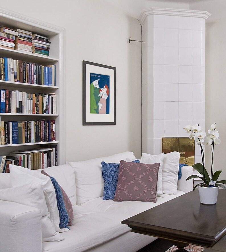 May include: A white couch with pillows in shades of blue and pink, a dark wood coffee table, and a framed poster on the wall. The poster features a blue background with a couple kissing in a green and pink design. The text on the poster reads "Dance and Sing".