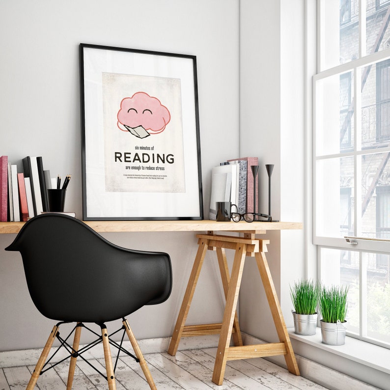 K&ouml;nnte beinhalten: Gerahmtes Poster mit dem Text "six minutes of READING are enough to reduce stress" und einer rosa Gehirngrafik. Das Poster befindet sich auf einem Holztisch mit einem schwarzen Stuhl, B&uuml;chern und einem Fenster mit Pflanzen.