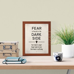 Op de afbeelding: Een ingelijst afdruk met een witte achtergrond en zwarte tekst die luidt: "FEAR is the path to the DARK SIDE. Fear leads to anger. Anger leads to hate. Hate leads to suffering."