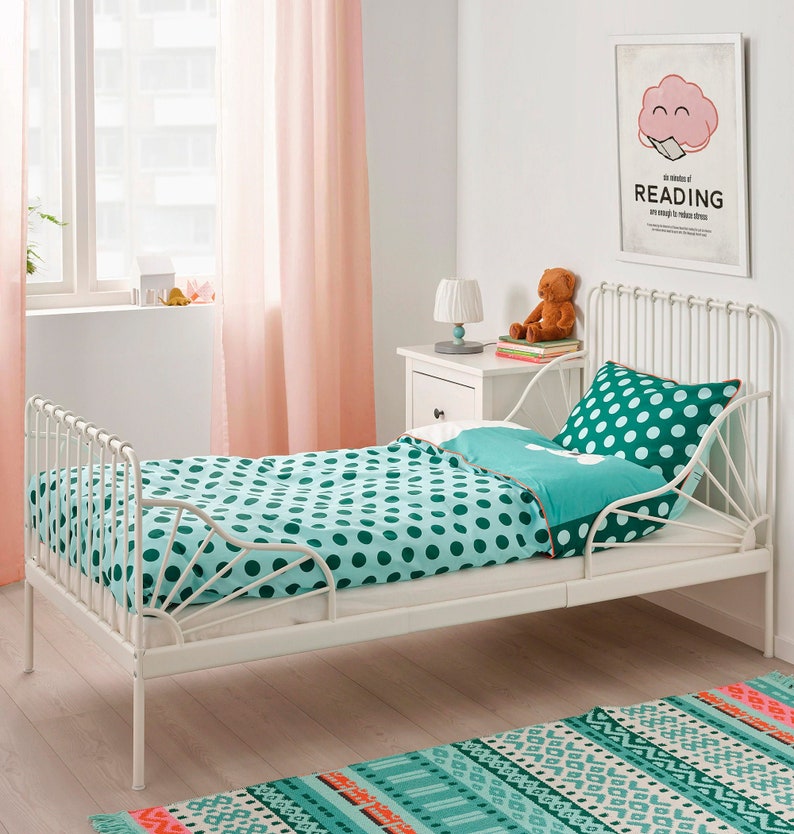 K&ouml;nnte beinhalten: Ein wei&szlig;es Metallbett mit einer t&uuml;rkis-wei&szlig;en Polka-Dot-Bettdecke und einem Kissen. Der Raum hat rosa Vorh&auml;nge, einen wei&szlig;en Nachttisch und einen gerahmten Druck mit der Aufschrift "Six minutes of READING are enough to reduce stress."