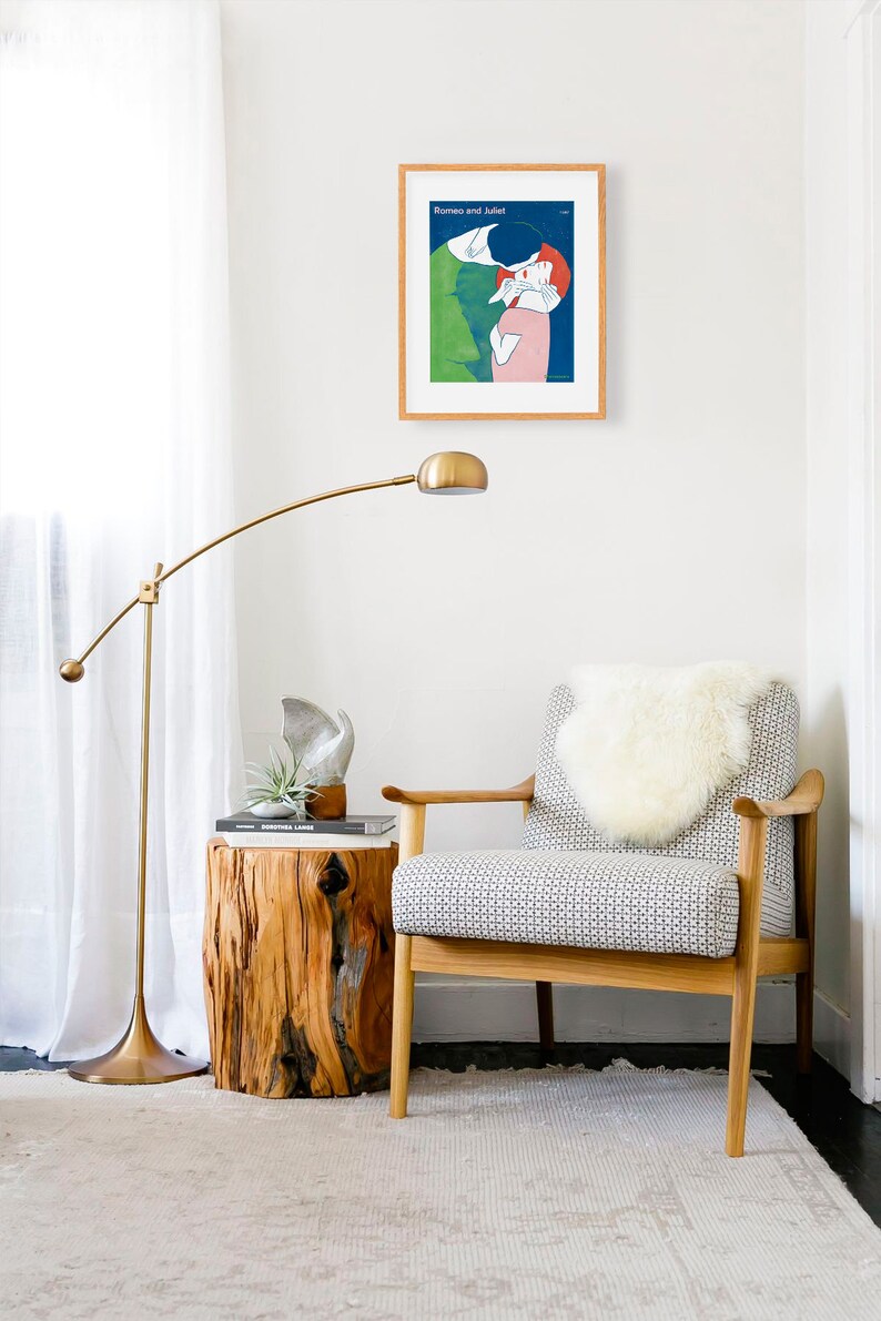 May include: A white armchair with a sheepskin throw pillow sits in a living room with a wooden side table, a gold floor lamp, and a framed poster with the text "Romeo and Juliet" on the wall.