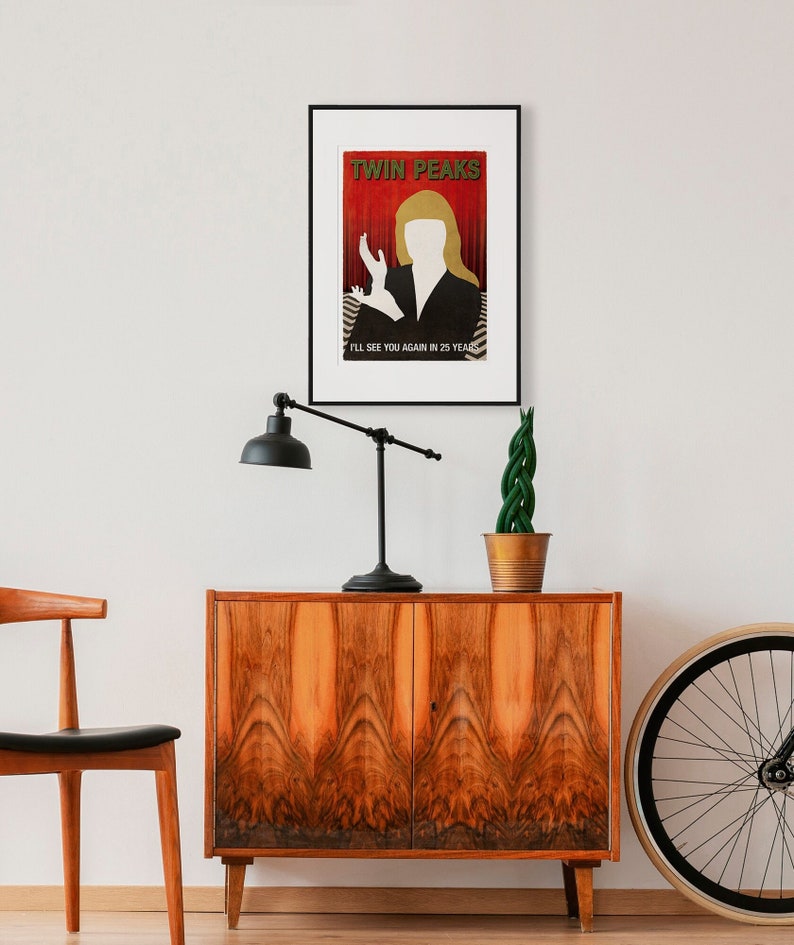 Op de afbeelding: Een ingelijste poster met een minimalistisch ontwerp met een silhouet van een vrouw met blond haar tegen een rode achtergrond. De poster luidt "Twin Peaks" en "Ik zie je over 25 jaar weer".