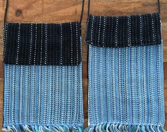 May include: Two woven crossbody bags. The bags have a rectangular shape with a flap at the top and a fringe at the bottom. The top flap is black with white dots, and the body is blue with vertical stripes. The bags have black straps.