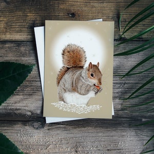 May include: A grey squirrel with a bushy tail sits on a snowy background and holds a nut in its paws. The squirrel is looking to the right. The background is a light brown with white snowflakes.