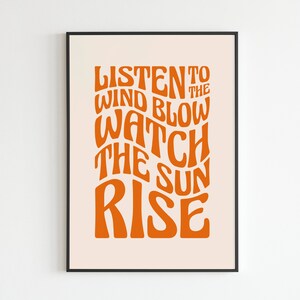 May include: Orange text on a light peach background in a black frame reads "Listen to the wind blow watch the sun rise".