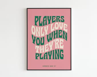 May include: A pink poster with a green and white text design that reads "Players only love you when they're playing". The poster is framed in black and has the text "Fleetwood Mac - Designs - 1977" at the bottom.