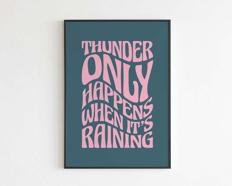 May include: A framed art print featuring the quote "THUNDER ONLY HAPPENS WHEN IT'S RAINING" in pink, stylized lettering. The text is set against a dark teal background, with a black frame.
