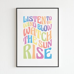 May include: A colorful typography print with the text "Listen to the wind blow watch the sun rise". The text is in a rainbow of colors, including pink, yellow, blue, green, and orange.