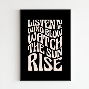 May include: Black and white typography poster with the text "Listen to the wind blow watch the sun rise" in a retro style.