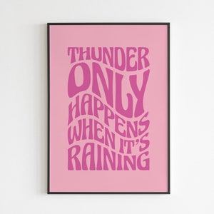 May include: A pink art print featuring the phrase "THUNDER ONLY HAPPENS WHEN IT'S RAINING" in a retro, wavy font. The text is a darker pink shade against a lighter pink backdrop, framed in black.