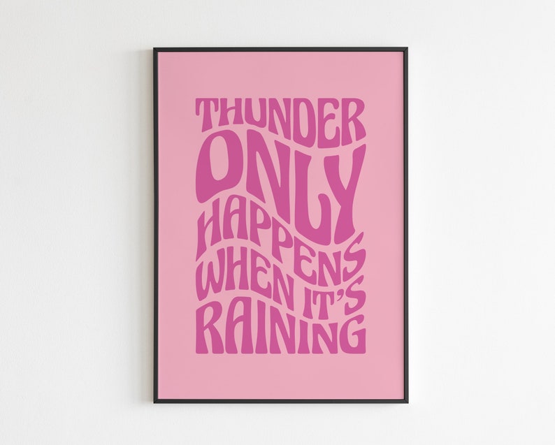May include: A pink art print featuring the phrase "THUNDER ONLY HAPPENS WHEN IT'S RAINING" in a retro, wavy font. The text is a darker pink shade against a lighter pink backdrop, framed in black.