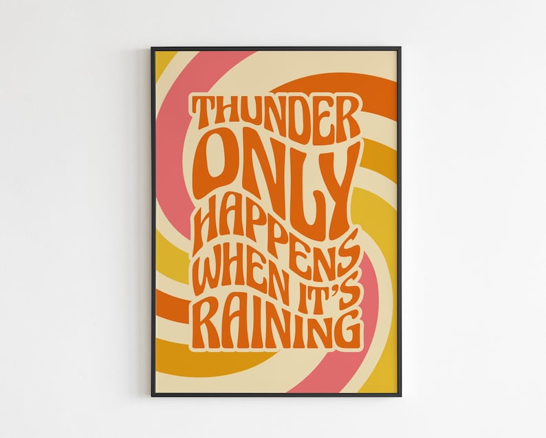 May include: A framed art print featuring the quote "THUNDER ONLY HAPPENS WHEN IT'S RAINING" in orange. The text is set against a swirling backdrop of pink, yellow, and cream. The design has a retro, vintage style.