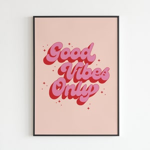 May include: A pink and red print with the text "Good Vibes Only" in a retro font style. The print is on a light pink background and is framed in a black frame.