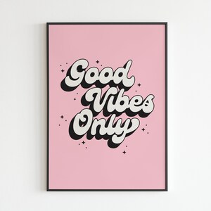 May include: A pink poster with black and white text that reads "Good Vibes Only" with a retro font style. The poster has a black frame.