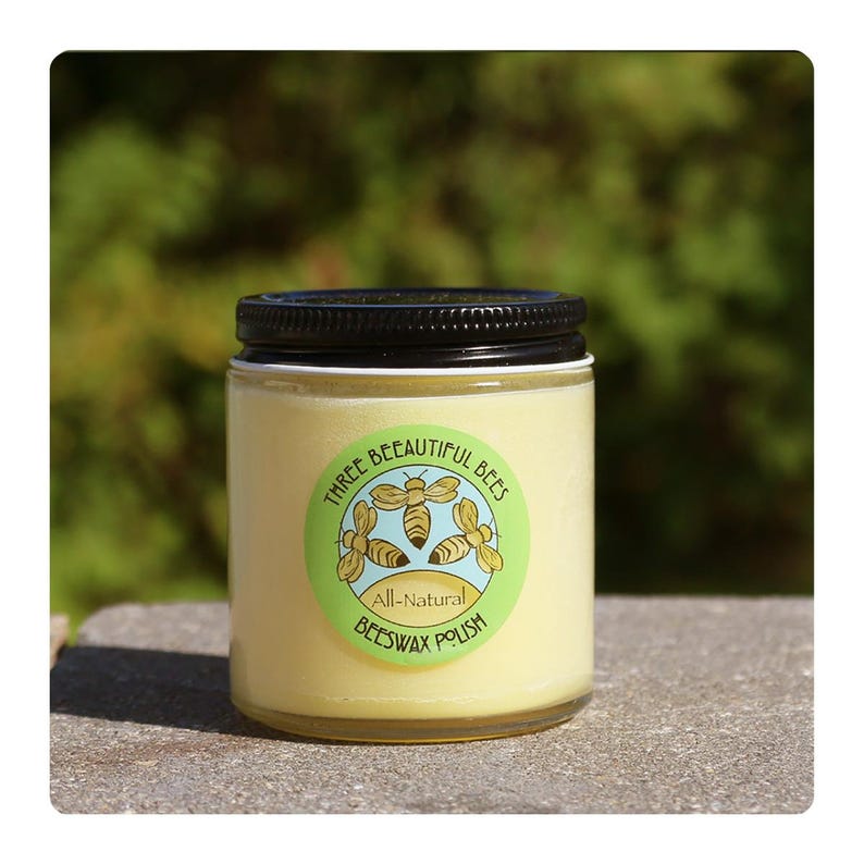 Może przedstawiać: Szklany słoik z czarną pokrywką i ż&oacute;łtą etykietą z napisem "Three Beautiful Bees All-Natural Beeswax Polish" z grafiką trzech pszcz&oacute;ł.