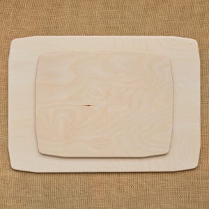 May include: Two light-colored wooden serving trays, one rectangular and one smaller, nested inside the larger one. The wood grain is visible, and the edges are rounded. The trays are likely for serving food or displaying items.