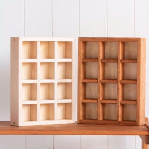 May include: Two wooden display shelves with a grid of twelve compartments each. One shelf is light-colored, the other is a warm brown. The shelves are sitting on a wooden surface against a white background.