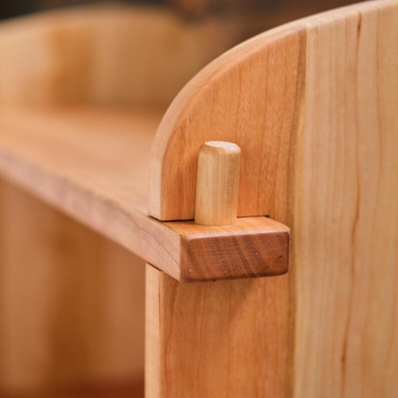 以下が含まれることがあります： 自然な仕上げのウッドシェルフのクローズアップ。シェルフは無垢材で作られており、シンプルでエレガントなデザインです。シェルフは、シェルフの穴に挿入された木製のダボで支えられています。