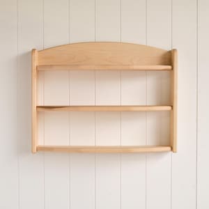 May include: A natural wood wall shelf with three shelves. The shelf has a curved top and is made of light wood.