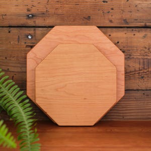 May include: Two octagonal wooden cutting boards, one slightly larger than the other, are stacked on top of each other. The boards are made of light brown wood and have a smooth, polished surface.