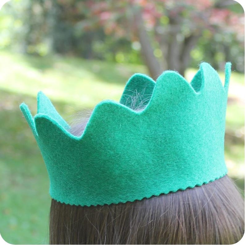 May include: A teal felt crown with a scalloped edge. The crown is worn on a person's head.