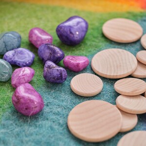 May include: A collection of purple, pink, and blue gemstones and wooden circles on a green and orange felt background.