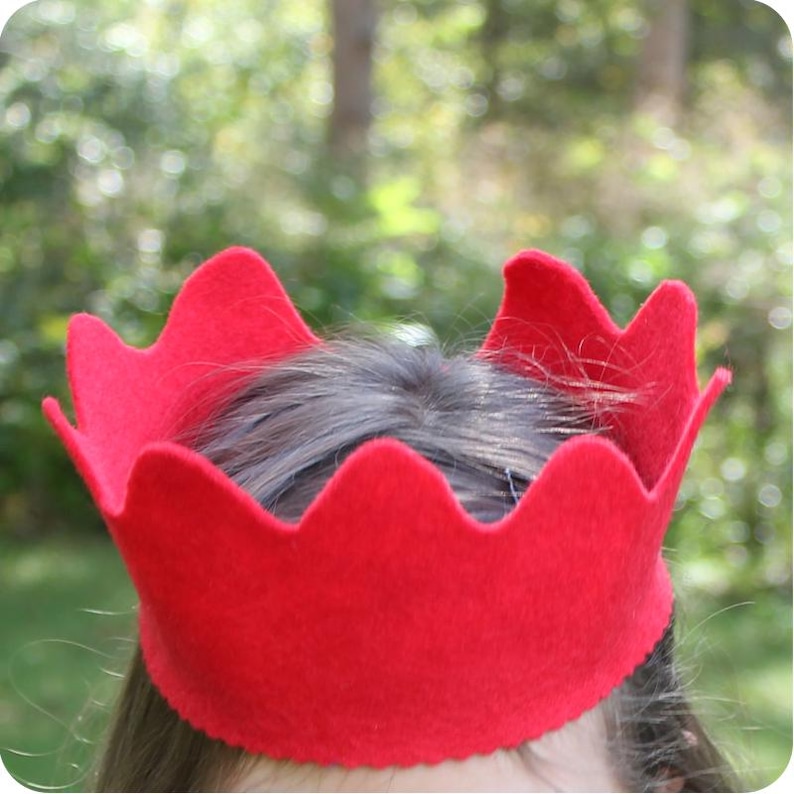 May include: A red felt crown with a scalloped edge. The crown is worn on a person's head.